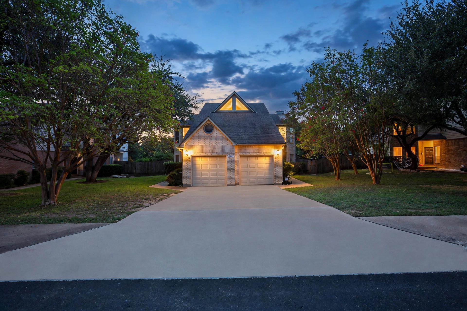 Mature trees frame the concrete driveway leading 