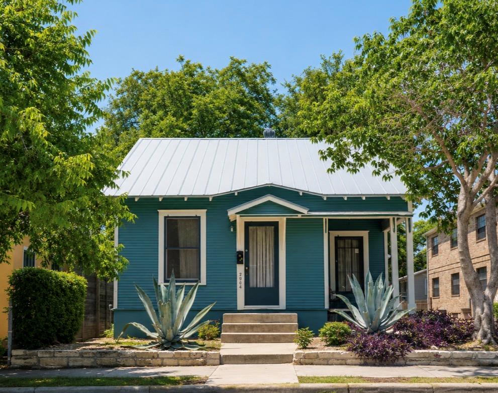 A charming teal bungalow, framed by lush foliage,