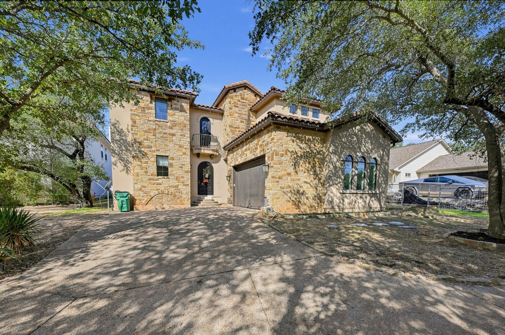 Lush mature trees frame a striking stone facade a